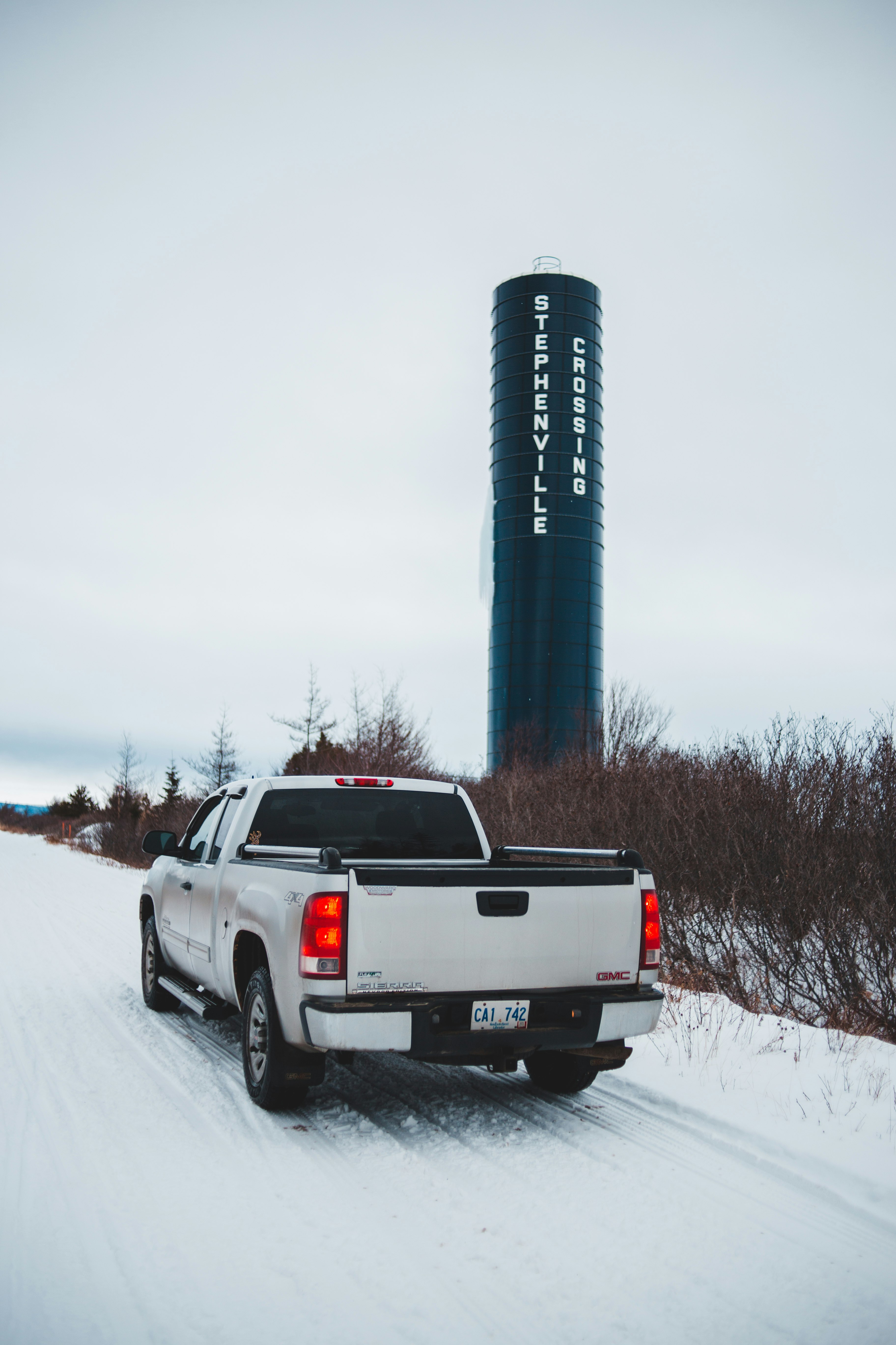 white pickup truck on snow covered road near shrubs and silo during day